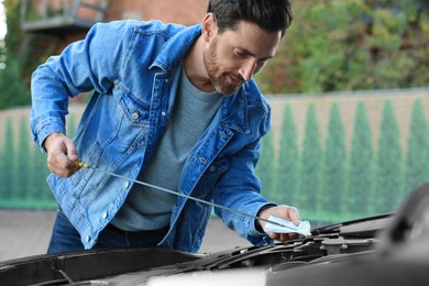 Man checking motor oil level with dipstick outdoors