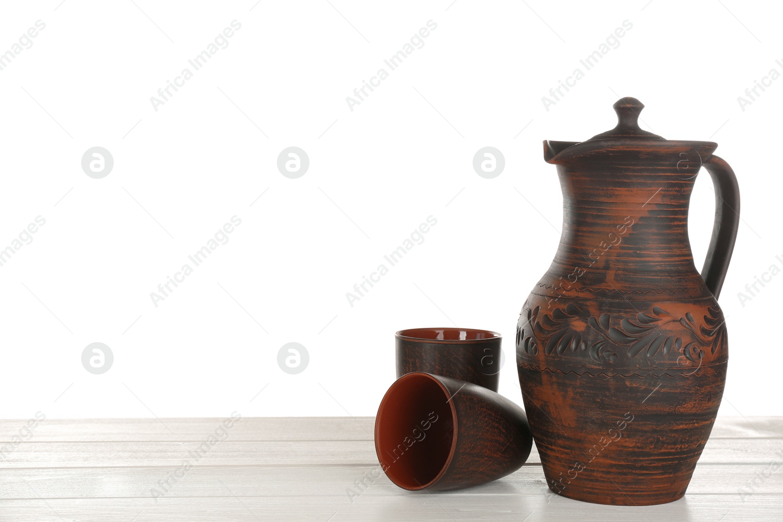 Photo of Clay jug and mugs on white wooden table