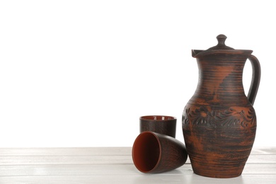 Clay jug and mugs on white wooden table