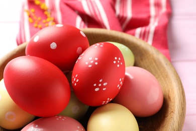 Photo of Bowl with colorful painted Easter eggs on table, closeup