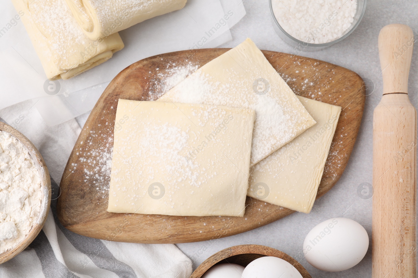 Photo of Raw puff pastry dough and ingredients on white table, flat lay