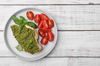Photo of Delicious chicken breast with pesto sauce, tomatoes and basil on white wooden table, top view. Space for text