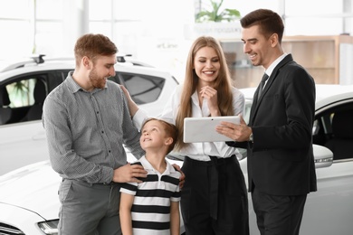 Salesman with tablet and young family in car salon