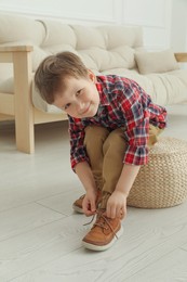 Photo of Cute little boy tying shoe laces at home