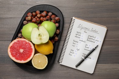 Notebook with products of low, moderate and high glycemic index, pen and food on wooden table, flat lay