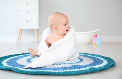 Photo of Cute little baby with soft towel on rug in bathroom
