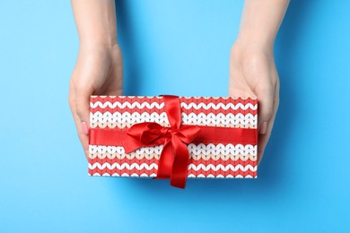 Photo of Christmas present. Woman holding beautifully wrapped gift box on light blue background, top view