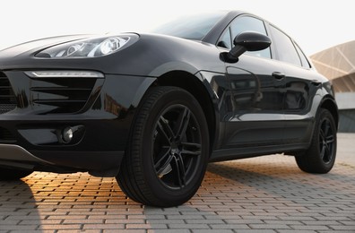 Photo of Modern black car parked on stone pavement outdoors