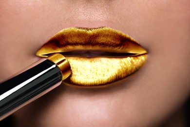 Young woman applying bright gold lipstick, closeup