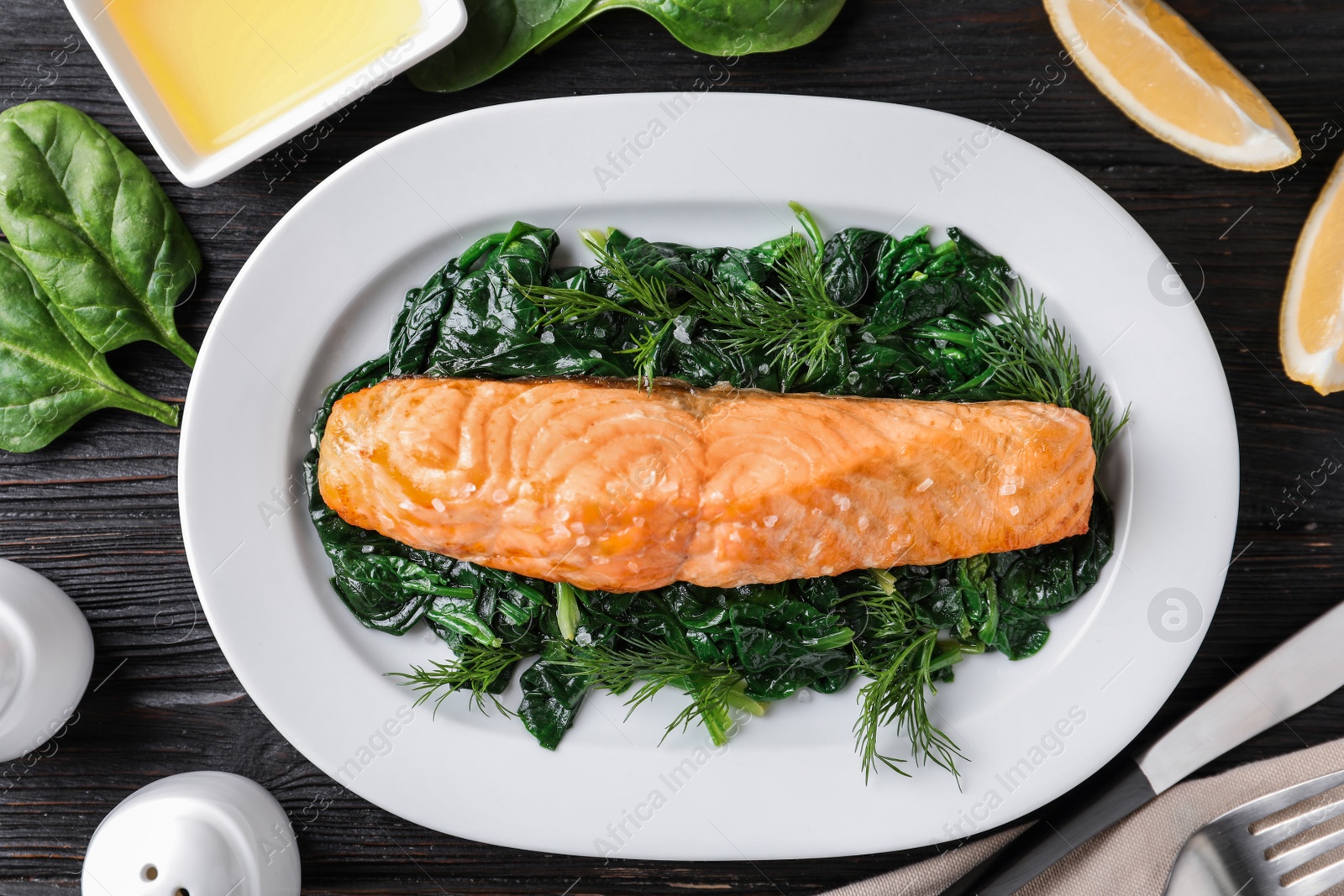 Photo of Tasty salmon with spinach on black wooden table, flat lay