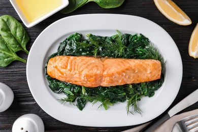 Photo of Tasty salmon with spinach on black wooden table, flat lay