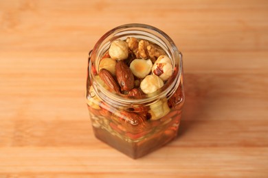 Photo of Different nuts and honey in jar on wooden table, above view