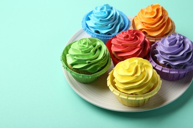 Photo of Plate with delicious bright cupcakes on turquoise background, closeup. Space for text