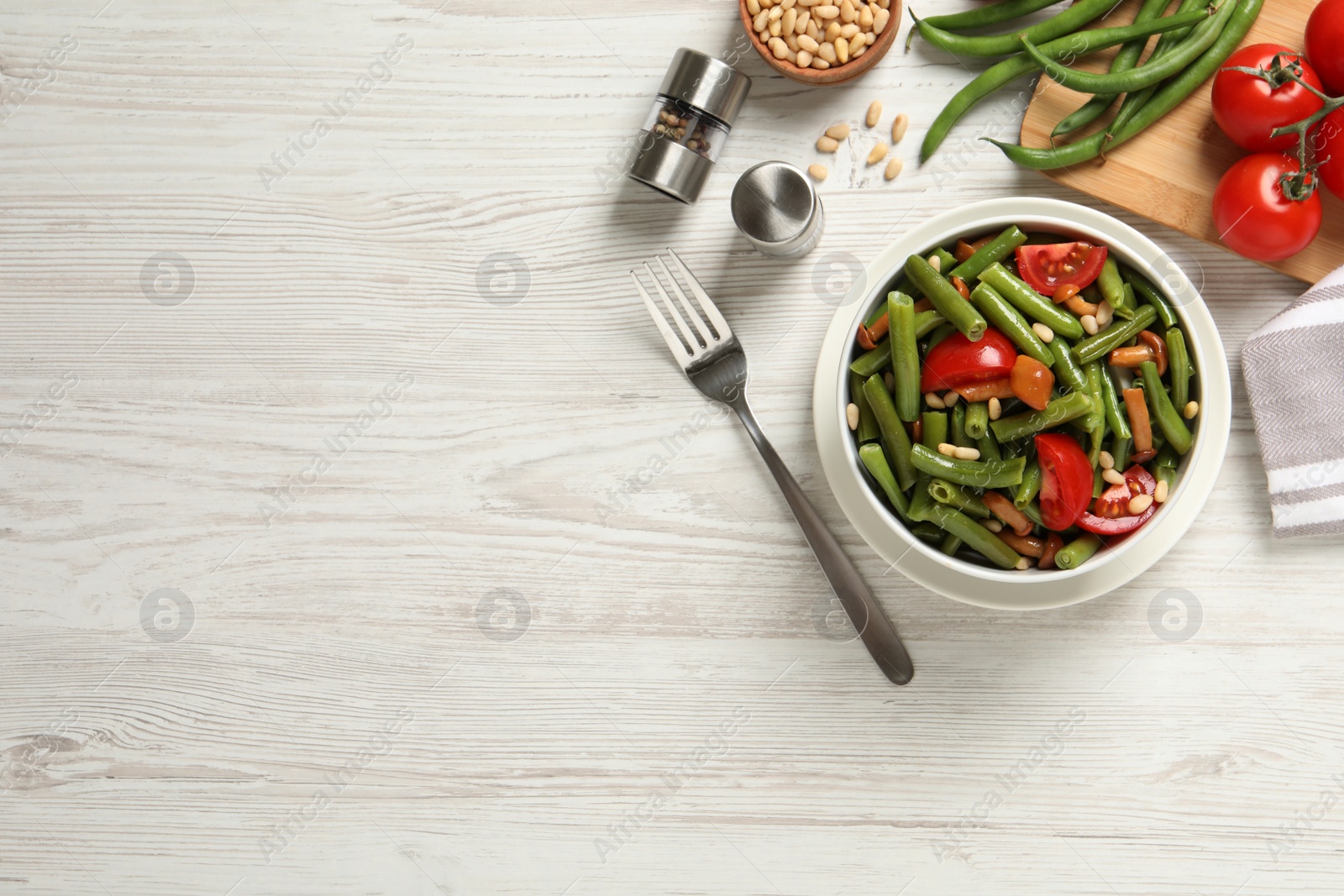 Photo of Delicious salad with green beans, mushrooms, pine nuts and tomatoes served on white wooden table, flat lay. Space for text