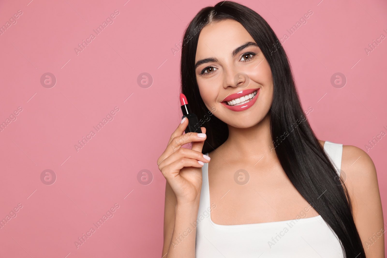 Photo of Young woman with beautiful makeup holding glossy lipstick on pink background, space for text