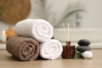Photo of Spa composition. Rolled towels, aroma diffuser, massage stones and burning candle on wooden table indoors