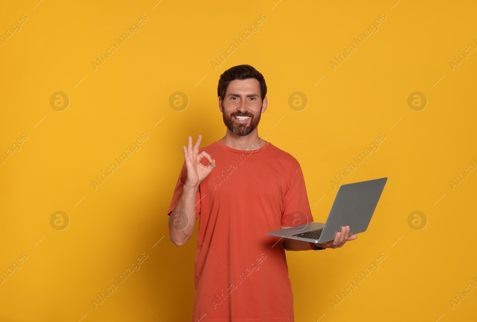 Photo of Handsome man with laptop showing OK gesture on orange background