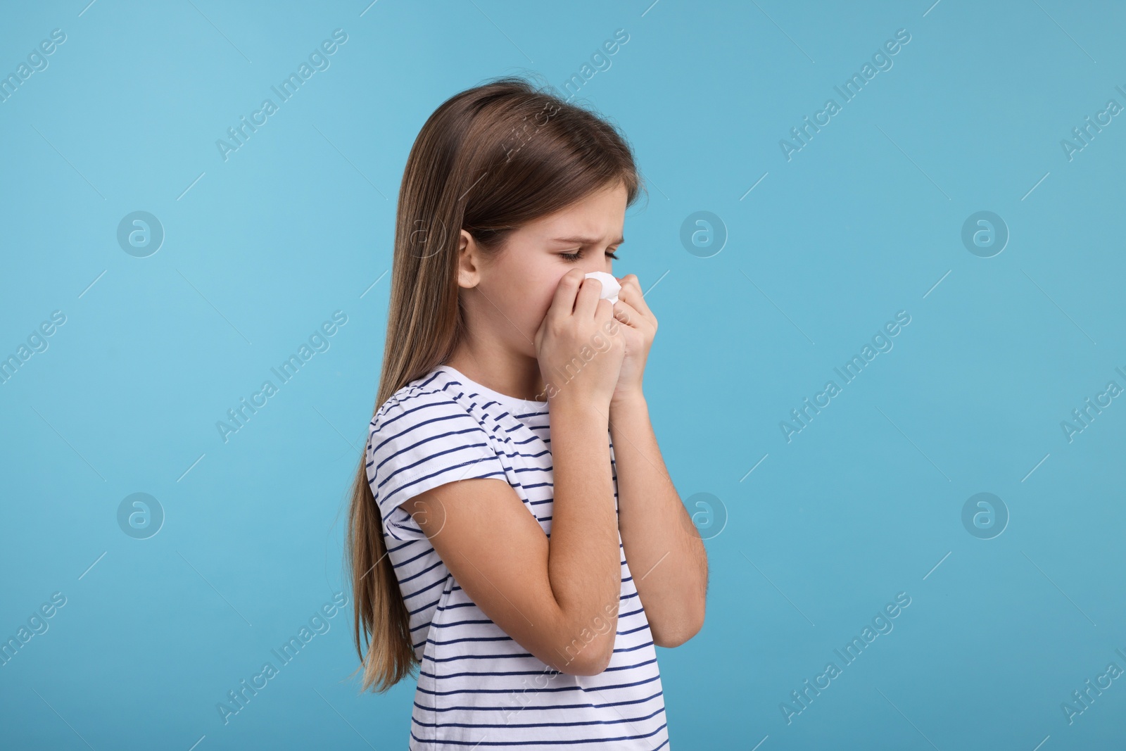 Photo of Sick girl with tissue coughing on light blue background