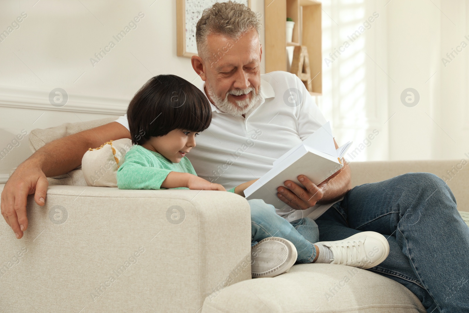 Photo of Happy grandfather with his grandson reading book together at home