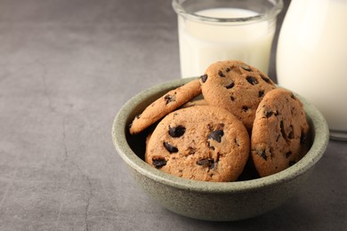 Photo of Delicious chocolate chip cookies and milk on grey table. Space for text