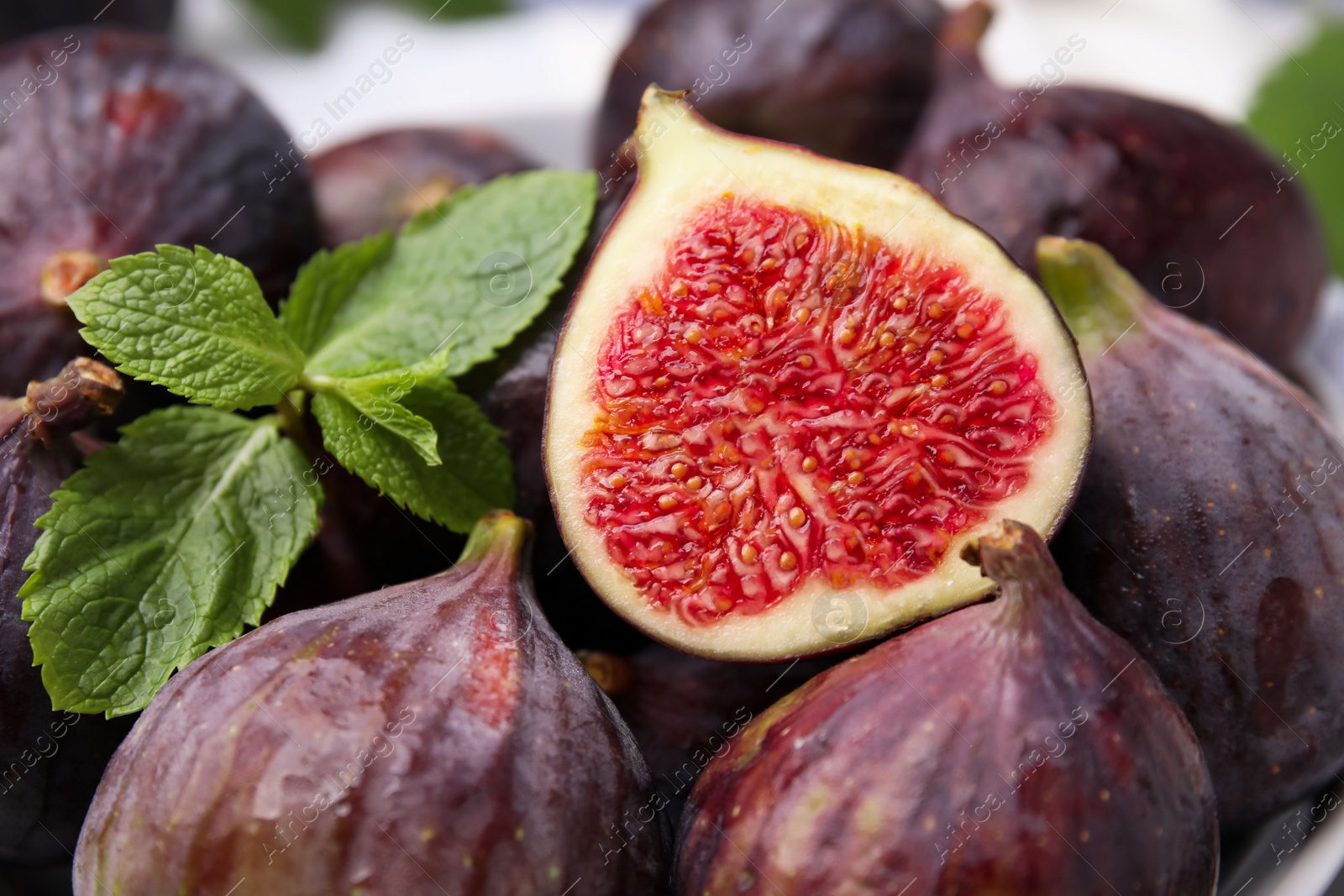 Photo of Tasty ripe figs and green mint leaves, closeup