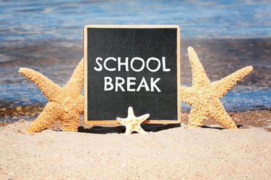 Image of Small black chalkboard with text School Break and starfishes on beach. Seasonal holidays 