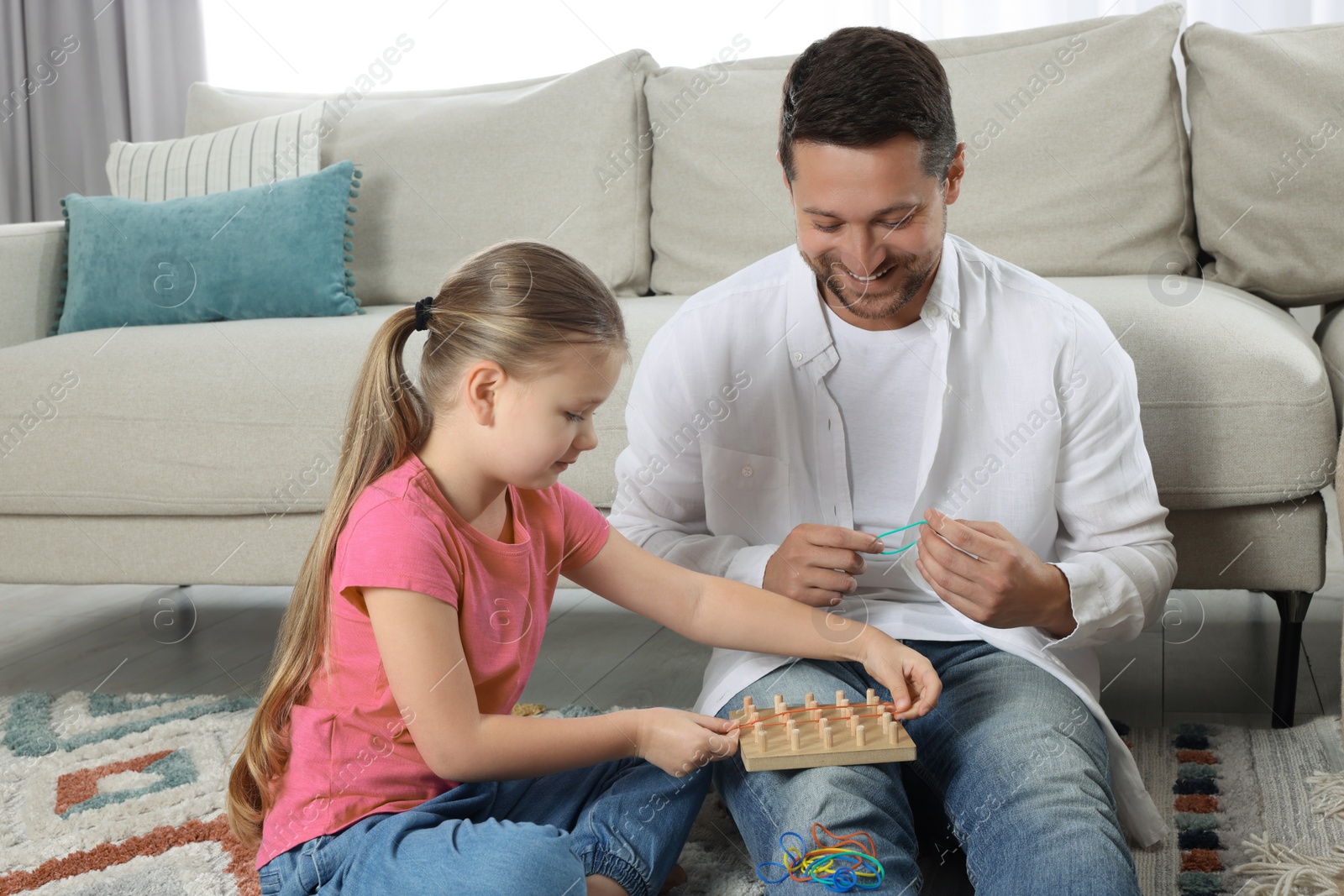 Photo of Motor skills development. Father helping his daughter to play with geoboard and rubber bands at home