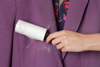 Woman removing hair from purple jacket with lint roller, closeup