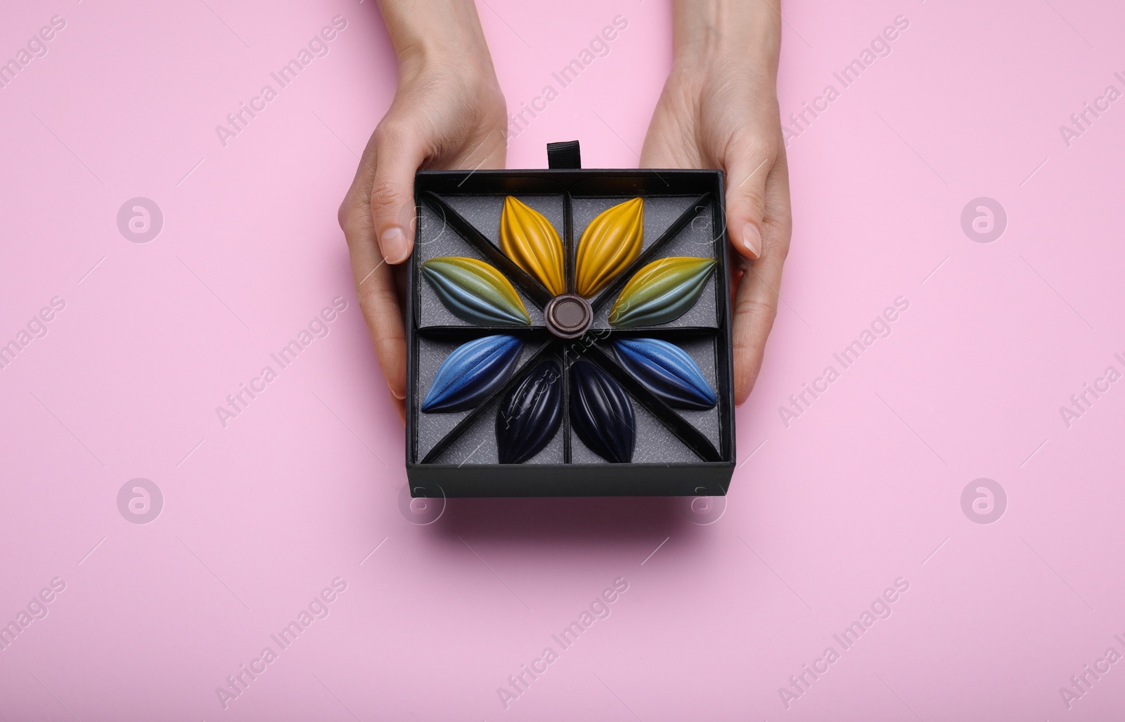 Photo of Woman with box of delicious chocolate candies on pink background, top view