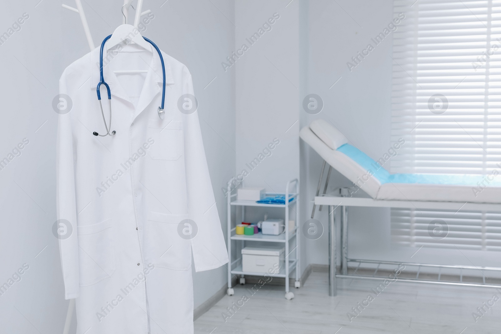 Photo of White doctor's gown and stethoscope hanging on rack in clinic. Space for text