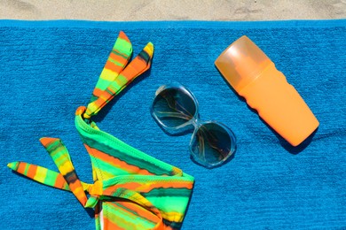 Photo of Soft blue beach towel with bottle of sunscreen, sunglasses and colorful bikini bottom, flat lay