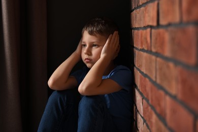 Photo of Child abuse. Upset boy near brick wall indoors