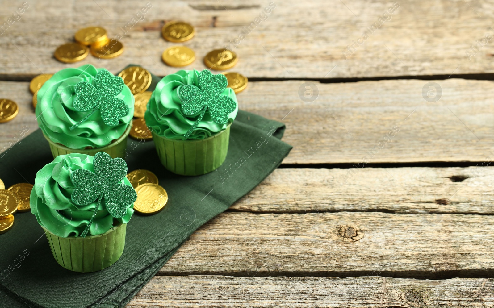 Photo of St. Patrick's day party. Tasty cupcakes with clover leaf toppers and green cream on wooden table. Space for text