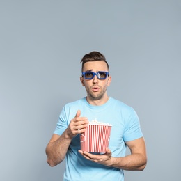 Emotional man with 3D glasses and popcorn during cinema show on grey background