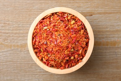 Photo of Aromatic spice. Red chili pepper flakes in bowl on wooden table, top view