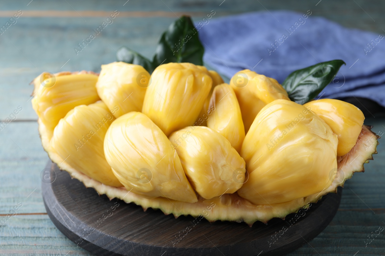 Photo of Fresh exotic jackfruit bulbs on light blue wooden table, closeup