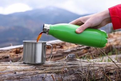 Photo of Woman pouring hot instant coffee from thermo bottle  into mug in mountains, closeup