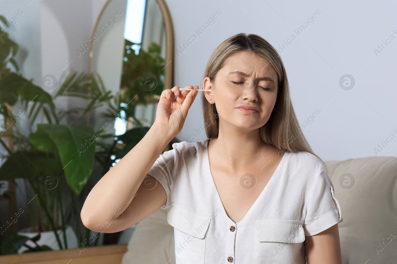 Photo of Young woman cleaning ear with cotton swab at home