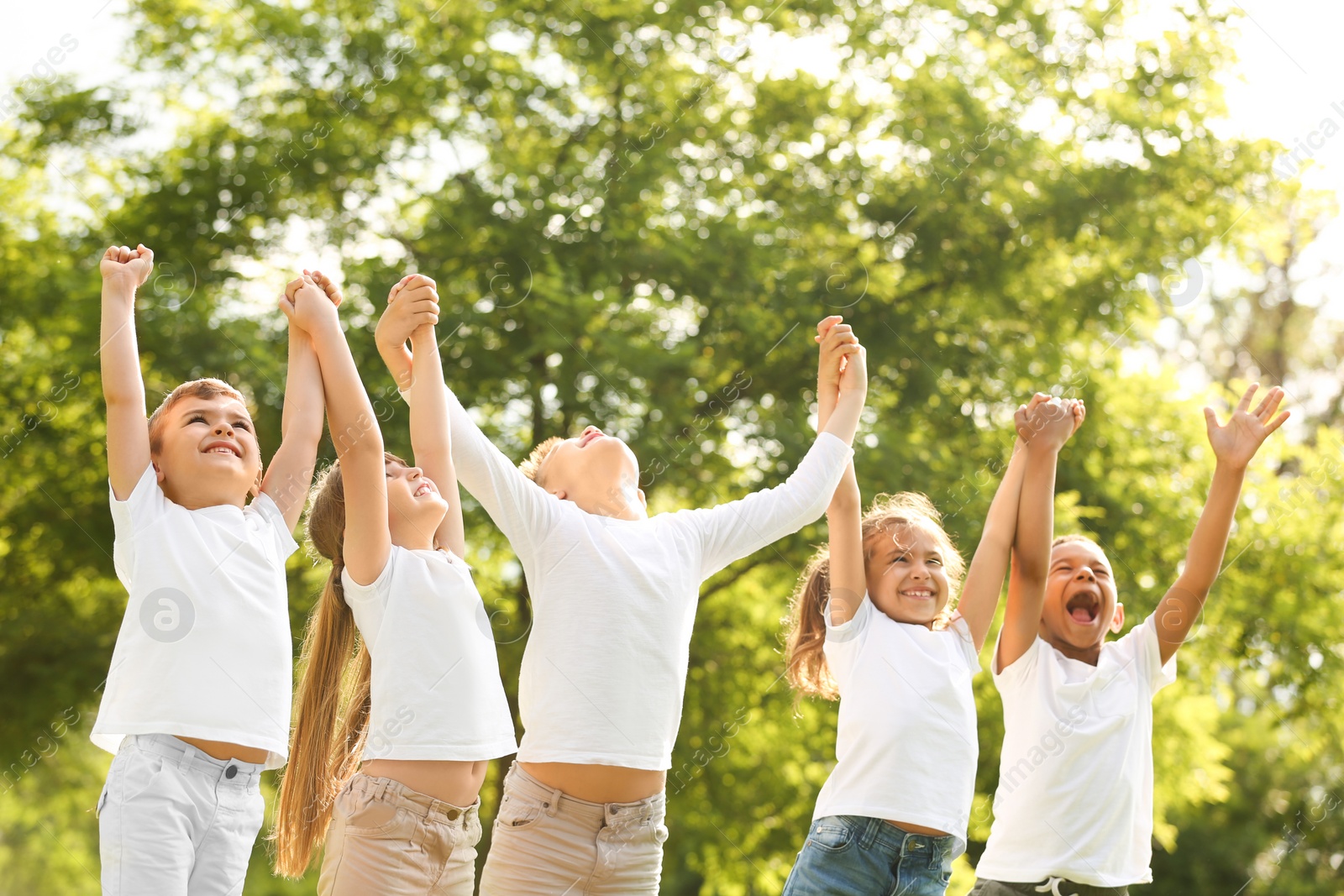 Photo of Group of children holding hands up in park. Volunteer project