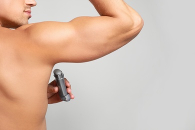 Young man applying deodorant to armpit on light background, closeup. Space for text