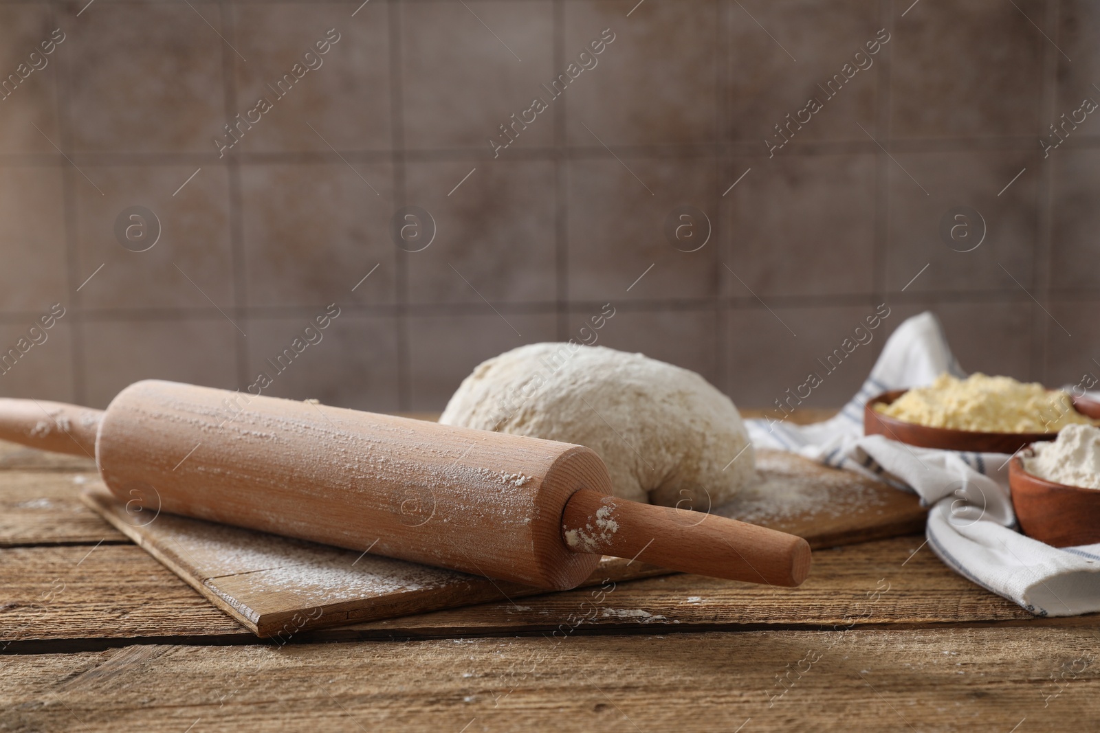Photo of Rolling pin, flour and dough on wooden table. Space for text