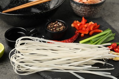 Different products and wok with chopsticks on dark table, closeup
