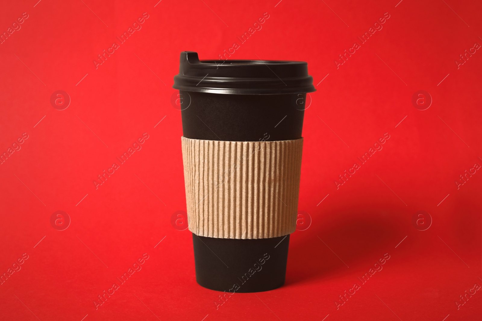 Photo of Takeaway paper coffee cup with cardboard sleeve on red background, closeup