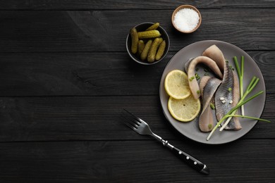Salted herring fillets served with green onions and lemon on dark wooden table, flat lay. Space for text