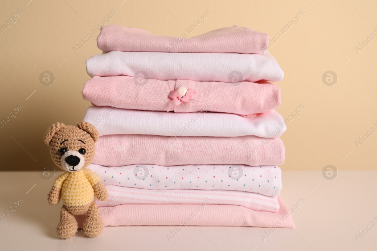 Photo of Stack of baby girl's clothes and toy bear on white table