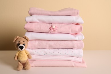 Photo of Stack of baby girl's clothes and toy bear on white table