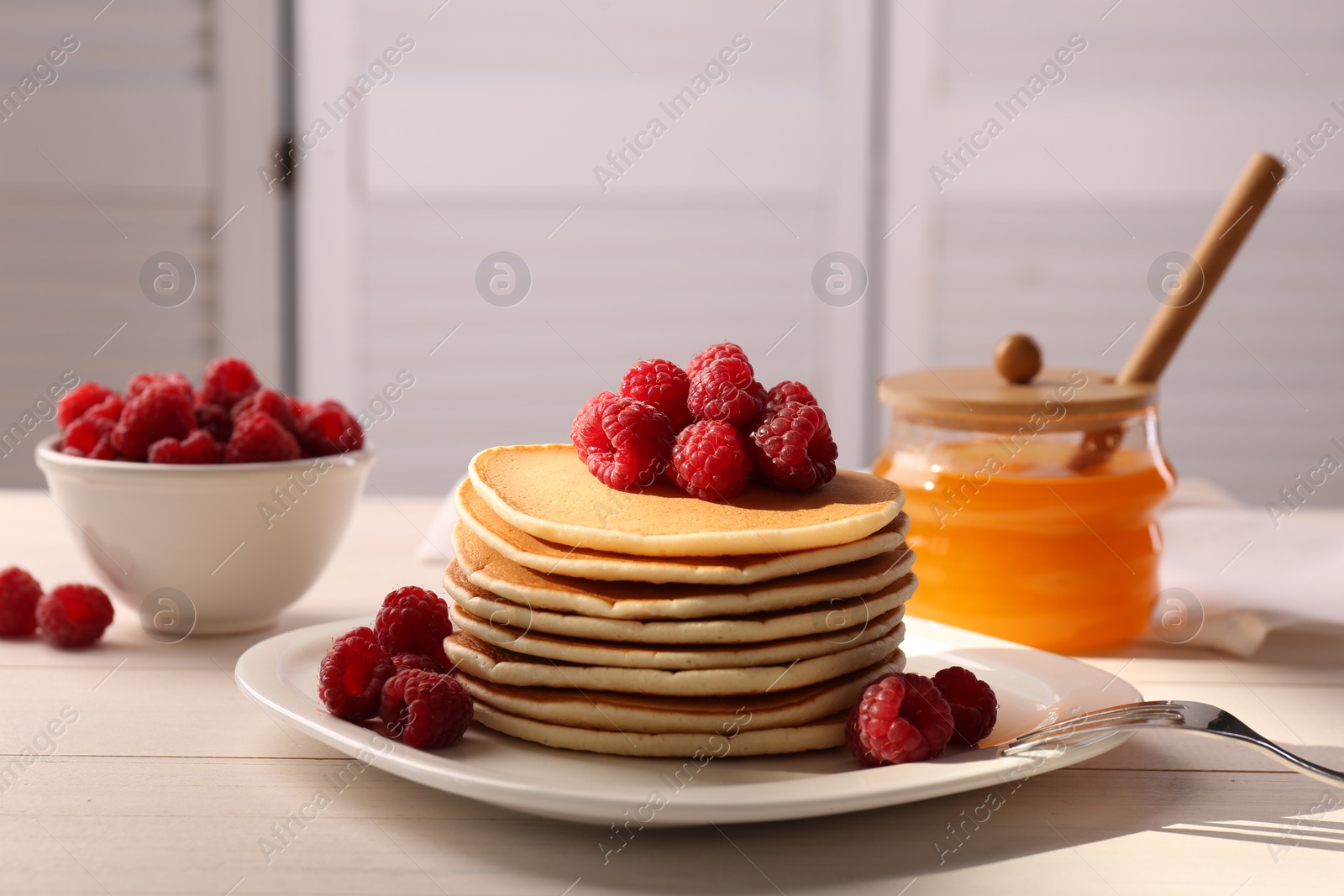 Photo of Stack of tasty pancakes with raspberries and fork on white wooden table
