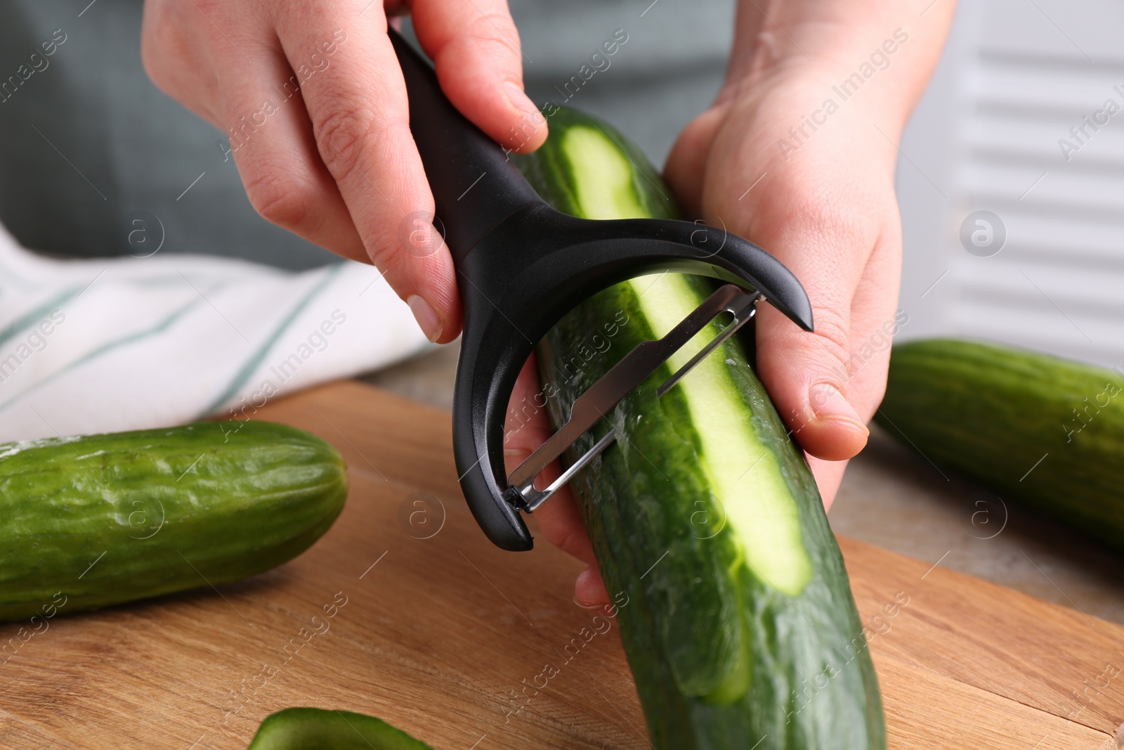 Photo of Woman peeling cucumber at wooden table indoors, closeup