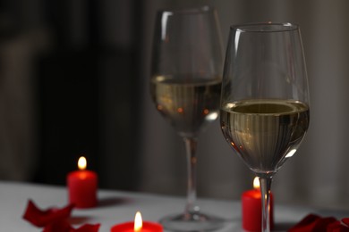 Glasses of white wine and burning candles on grey table against blurred background, space for text. Romantic atmosphere