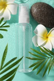 Wet bottle of micellar water, leaves, flowers and spa stones on turquoise background, flat lay